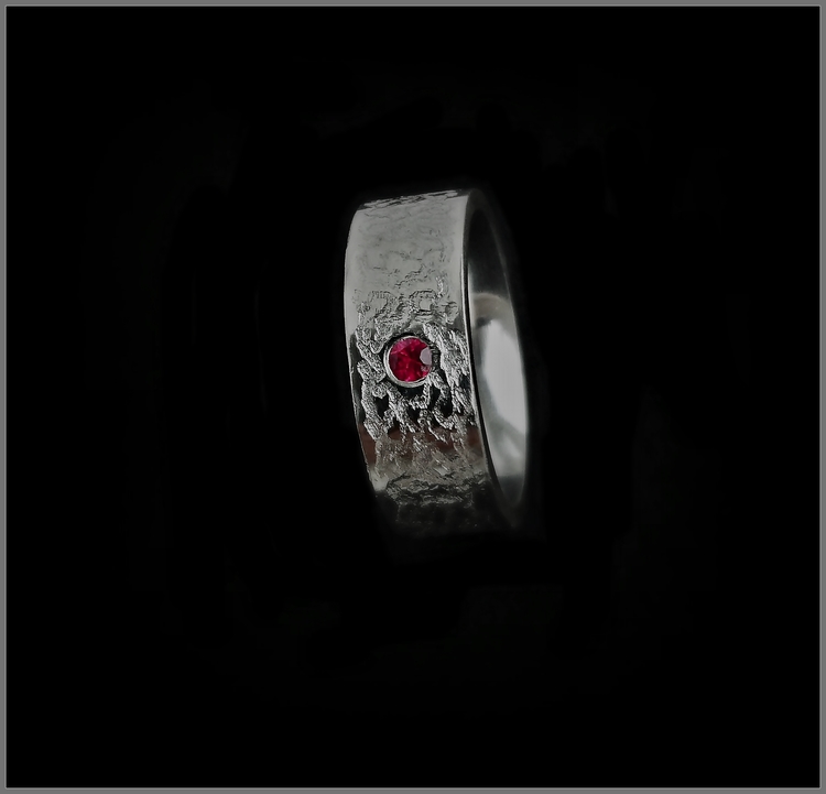 Sindre silverring med röd rubin på 0,10ct. Ytan har ett gåtfullt slingrande handarbetat mönster ingraverat i den flacka blanka ytan.