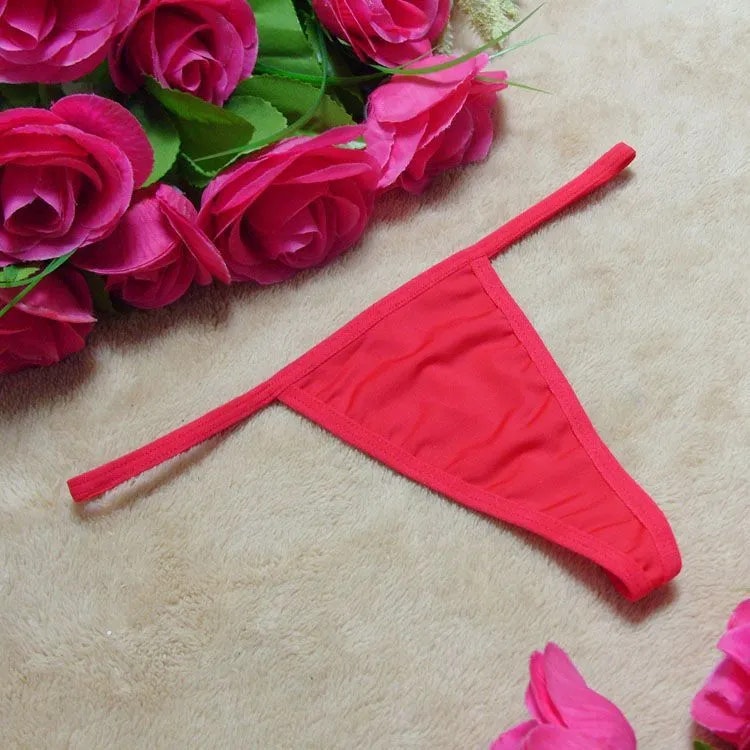 En röd stringtrosa presenterad bredvid ett bunt av förföriska rosa rosor på en mjuk yta, från Hot Woman Clothes kollektion av sexiga trosor.