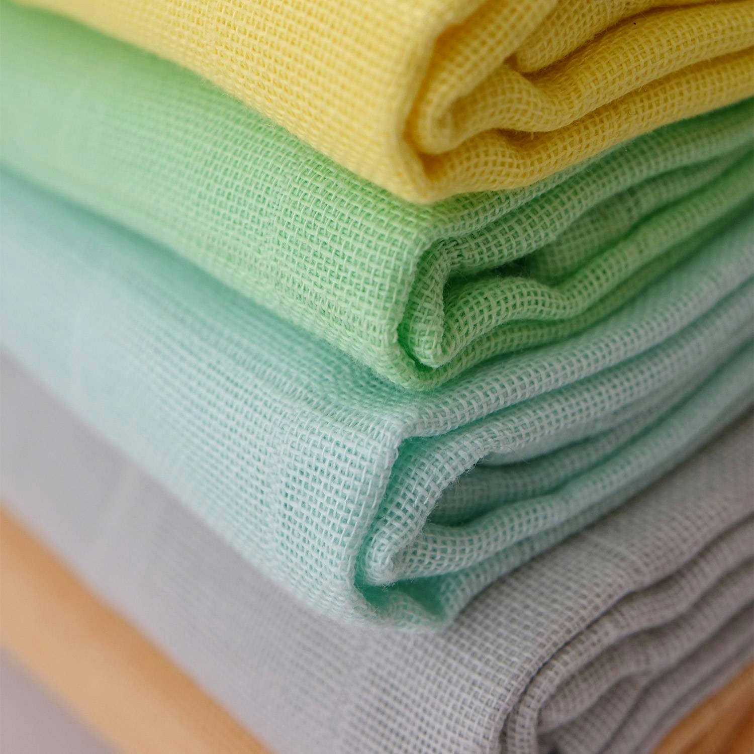 en närbild på en trave tygblöjor, i form av vikblöjor, i olika färger i ekologisk bomulsmuslin från Avo&Cado. A close-up of cloth diapers/flat diapers in different colors.