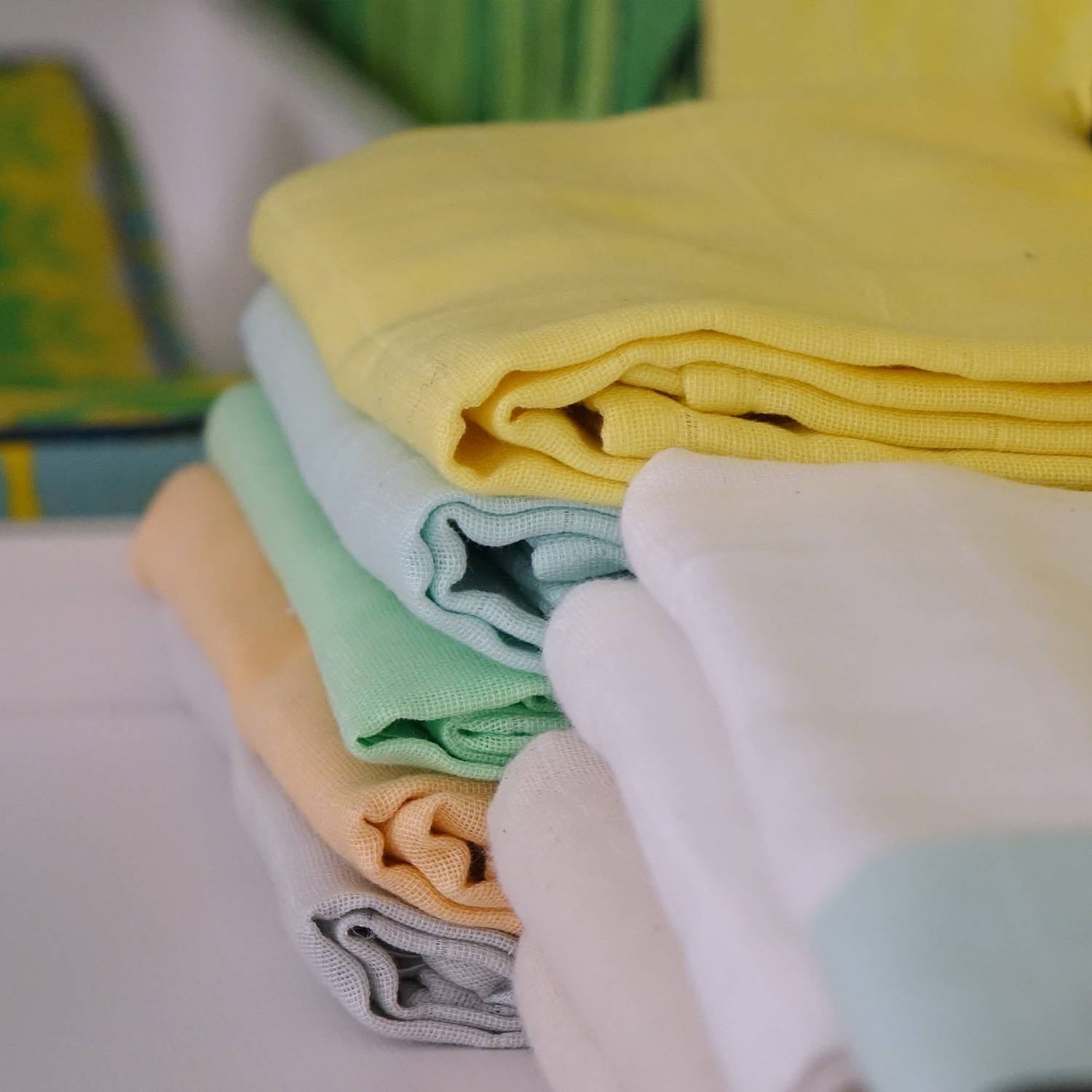 2 högar med tygblöjor i olika färger, i form av vikblöjor, i ekologiskt muslintyg från Avo&Cado. 2 piles of cloth diapers, in form of flat diapers in different colors.