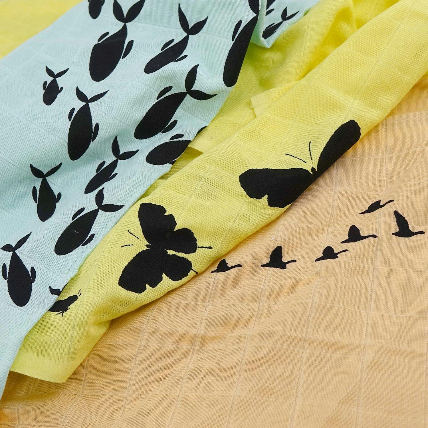 3 tygblöjor: en blå vikblöja med fiskar på, en gul vikblöja med fjärilar på, en orange vikblöja med flygande fåglar på. 3 cloth diapers in form of flat diapers in different colors and patterns.