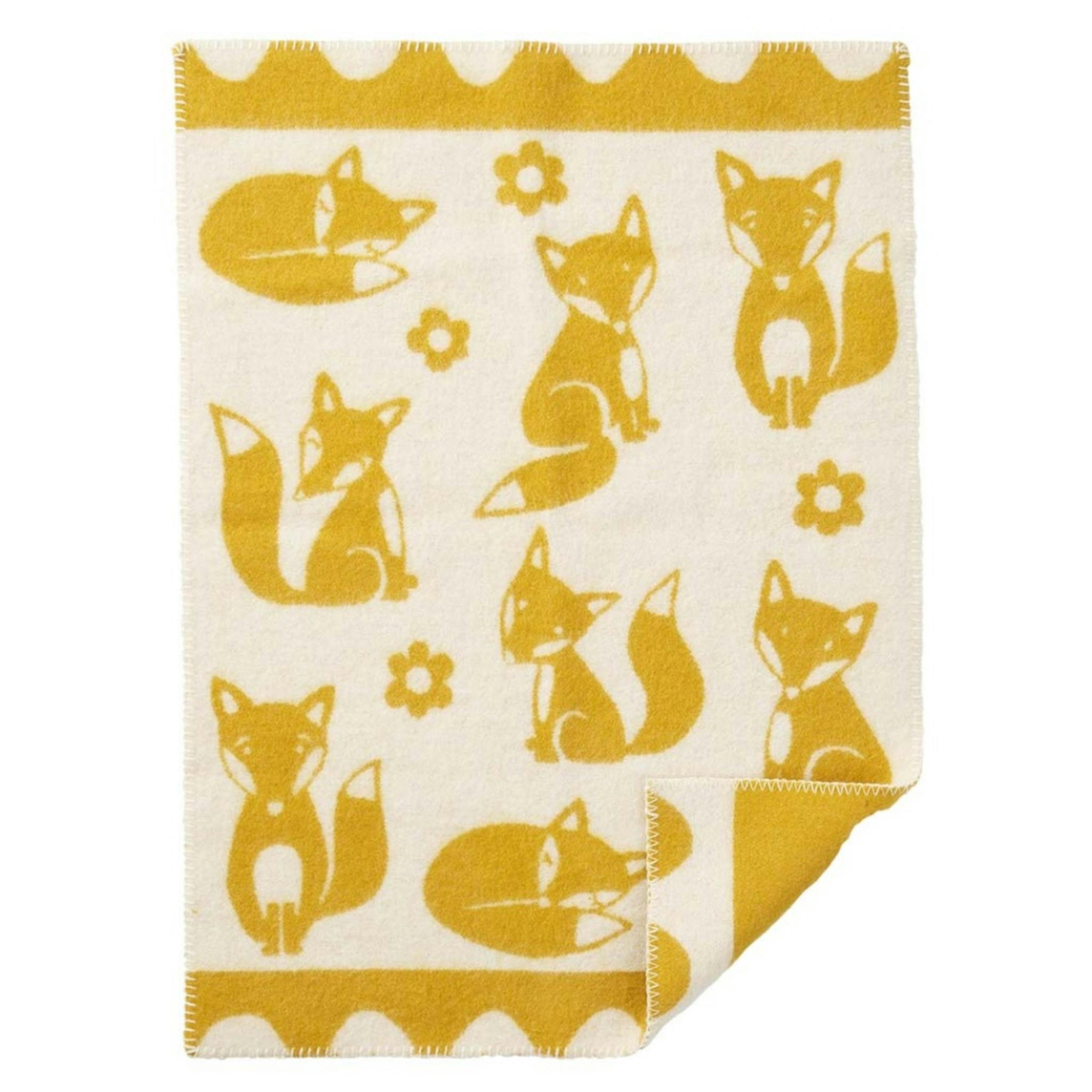 Fin gul filt i ull mönstrad med rävar från Klippan filten gör sig fin i spjälsängen.