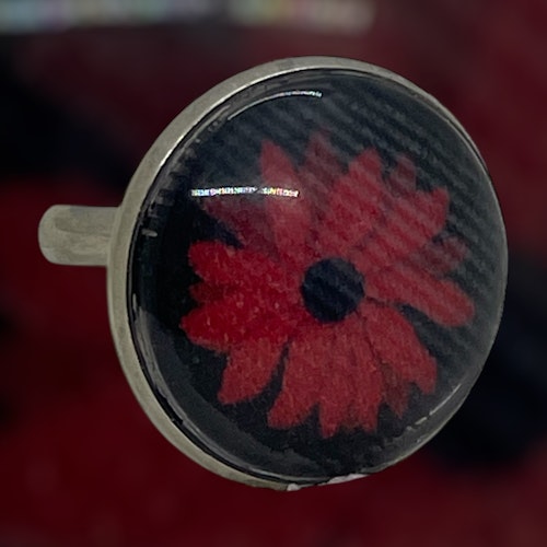 en stiliserad blomma på svart tyg i en cabochonring
