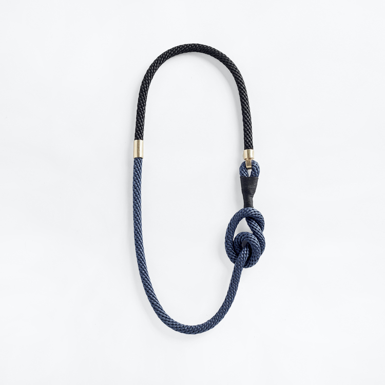 Halsband av svart och blått rep med en stor knut och ögla omlindad av svart vaxad bomullstråd. Symmetriska guldmetall-hakar på var sida.