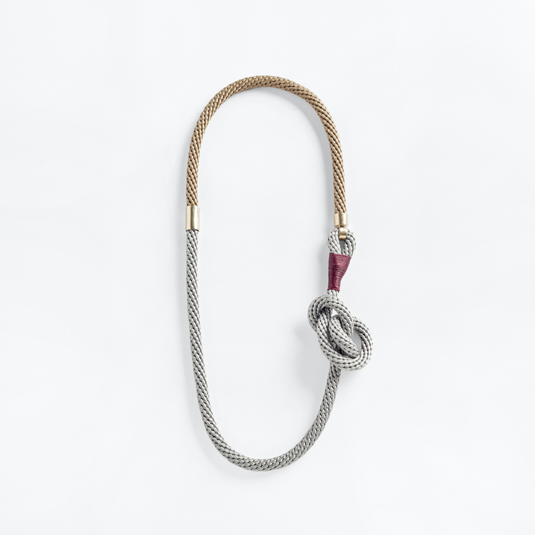 Halsband av beige och grått rep med stor knut och ögla omlindad av röd vaxad bomullstråd. Symmetriska guldmetall-hakar på var sida.