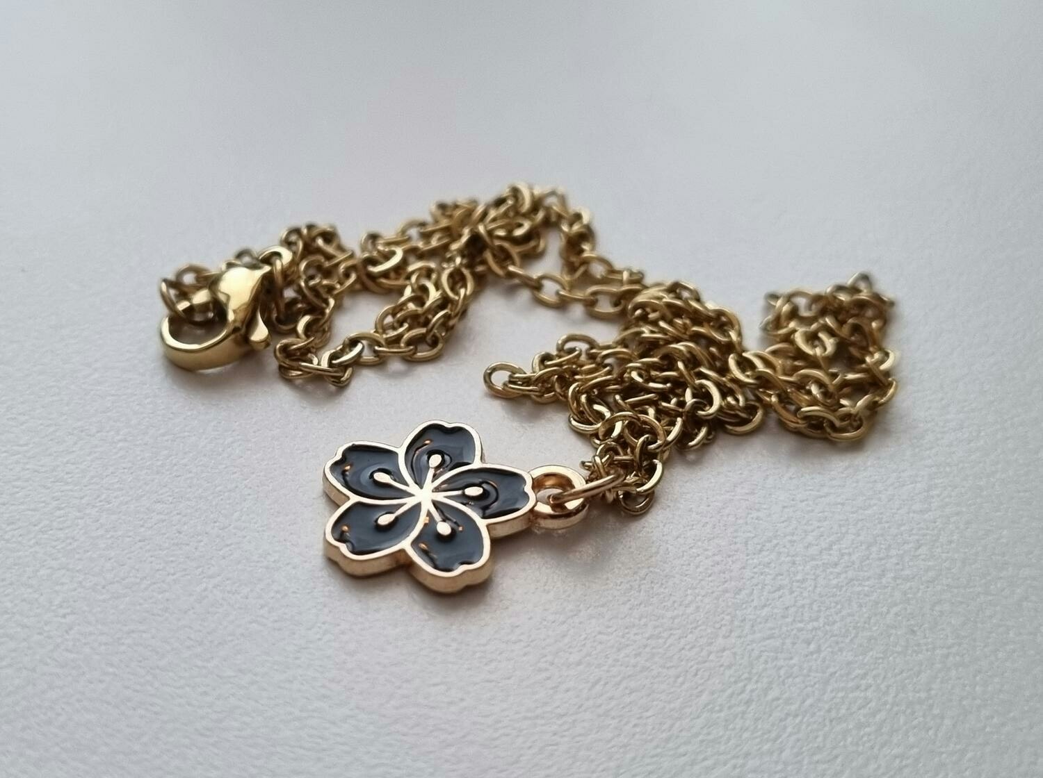 Guldfärgat halsband med en svart blomma