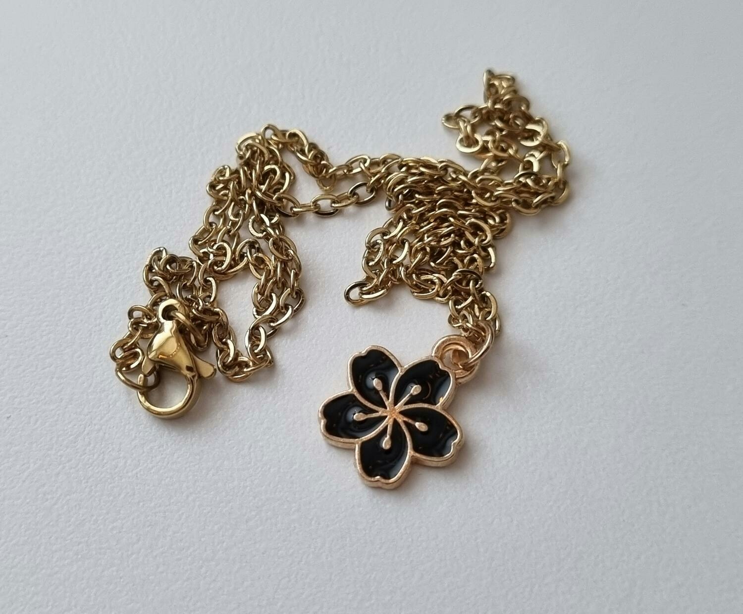 Guldfärgat halsband med en svart blomma