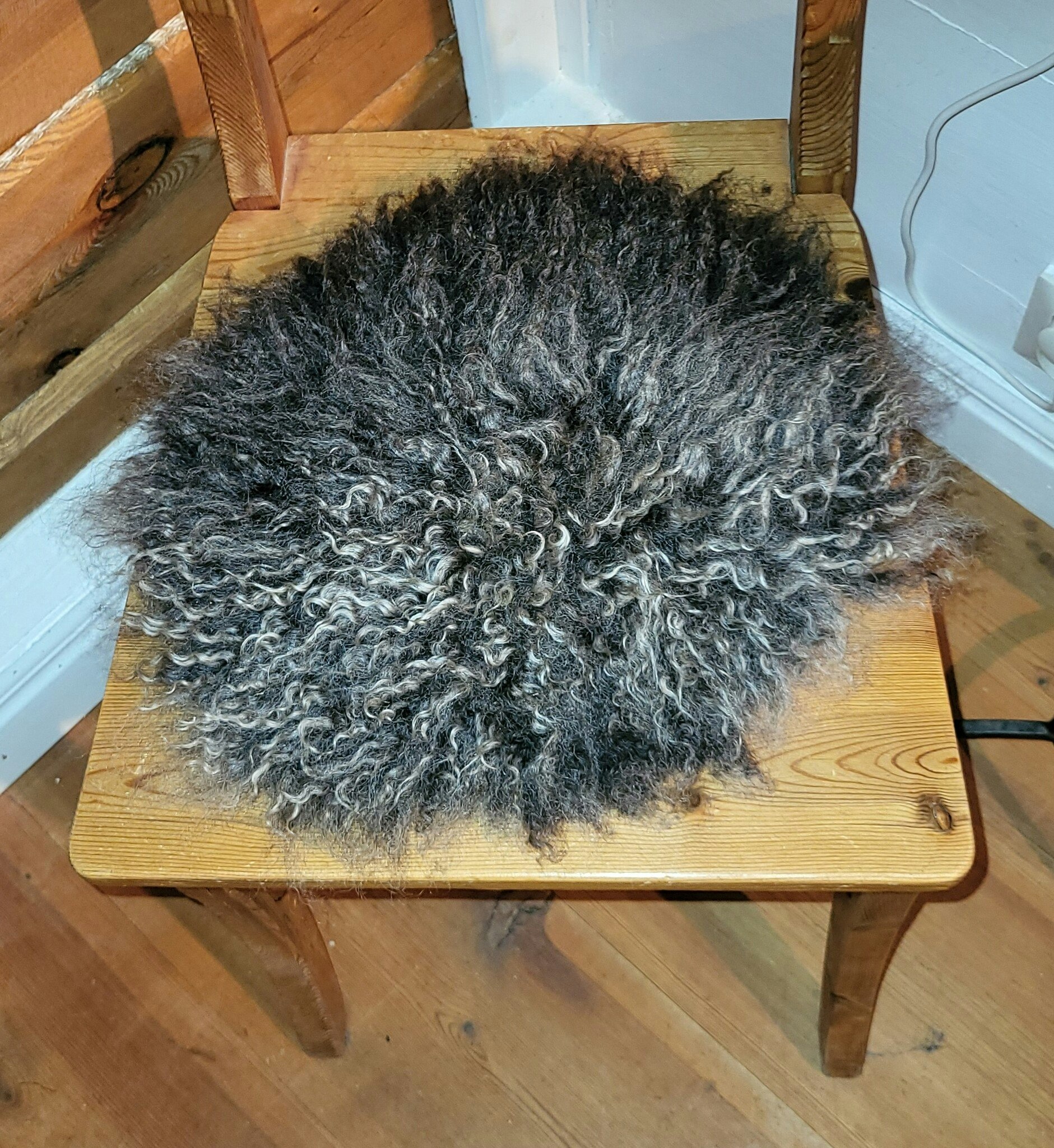 Stolsdyna av fårskinn, svart med silvergrå lockar.
