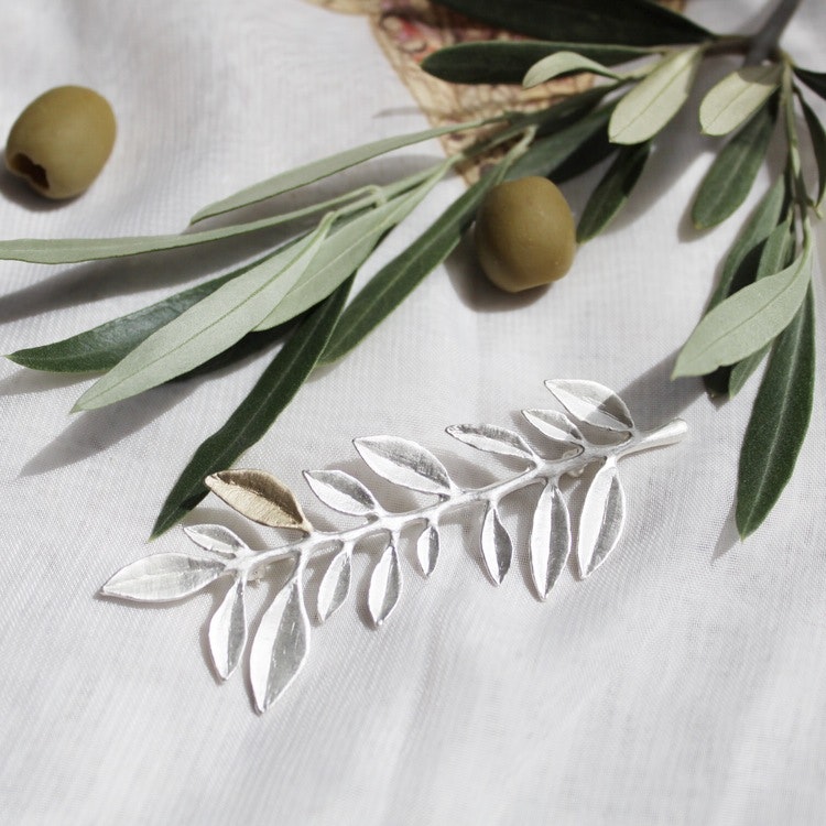 Olive Branch-broschen är en stilig och tidlös brosch föreställandes en olivkvist. Broschens motiv är tydligt inspirerad av naturens verkliga olivkvistar och bevarat i broschen finns olivbladets vackra