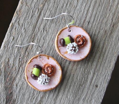 Örhängen, rosa fikatallrikar med dammsugare, chokladboll och kanelbulle