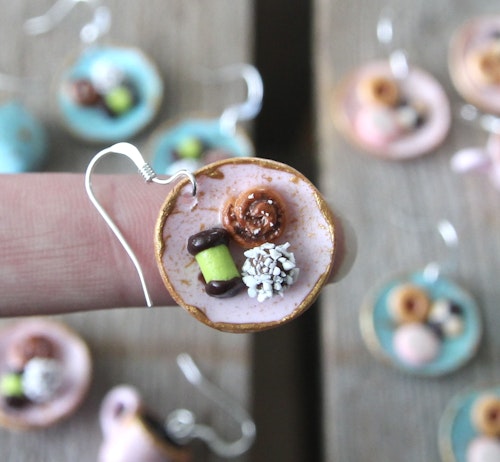 Örhängen, rosa fikatallrikar med dammsugare, chokladboll och kanelbulle