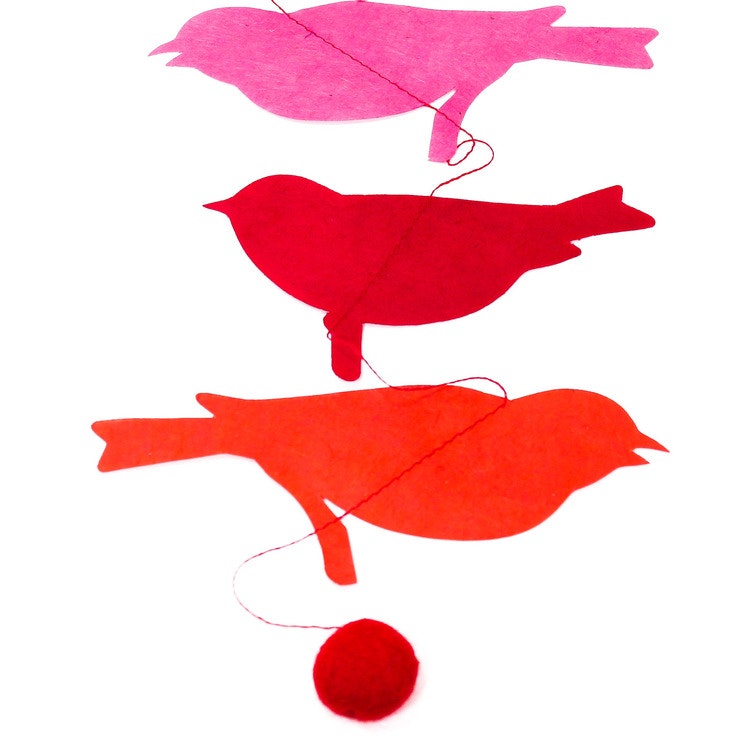 Girlang med pappersfåglar i olika röd/orange/rosa nyanser. Längst ner hänger en liten boll av tovad ull.