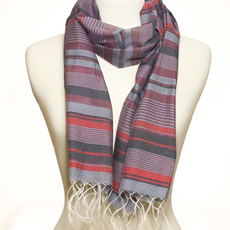 Randig sjal eller scarf i milda färger, röda, duvblå och mörkblå toner. 50 % siden, 50 % bomull. Halsduken är handvävd i Indien för Fair Trade.