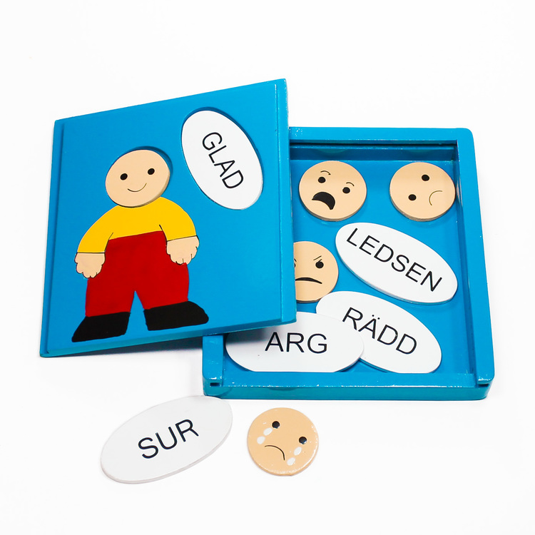 Träpussel i låda, motiv olika känslor. Ansiktsuttryck/emojis paras ihop med rätt ord: glad, ledsen, arg, sur, rädd. Öppen låda med pusselbitarna.