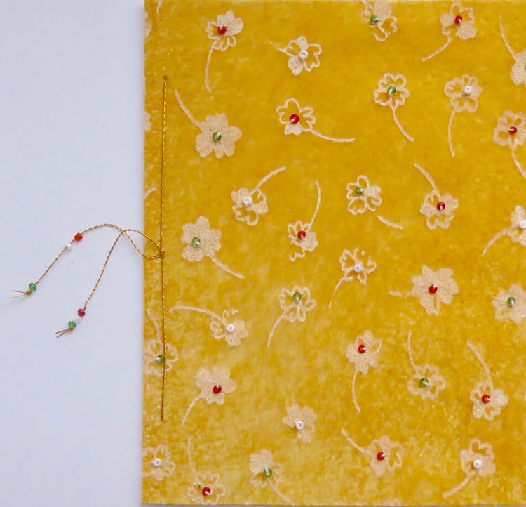 Vikt hälsningskort, på framsidan gult färgat och med målade små vita blommor som har små pärlor påsydda i mitten. Fastsydd pappersark att skriva på. Handgjort.