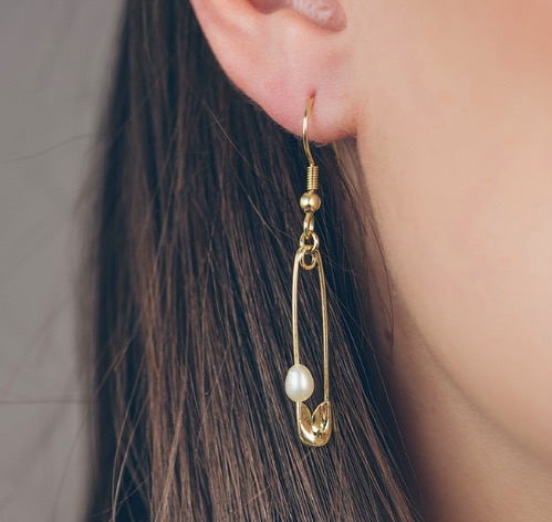 Örsmycke Säkerhetsnål i  guldgul färg, med vit pärla. Bilden visar hur örhänget ser ut när det bärs i örat.
