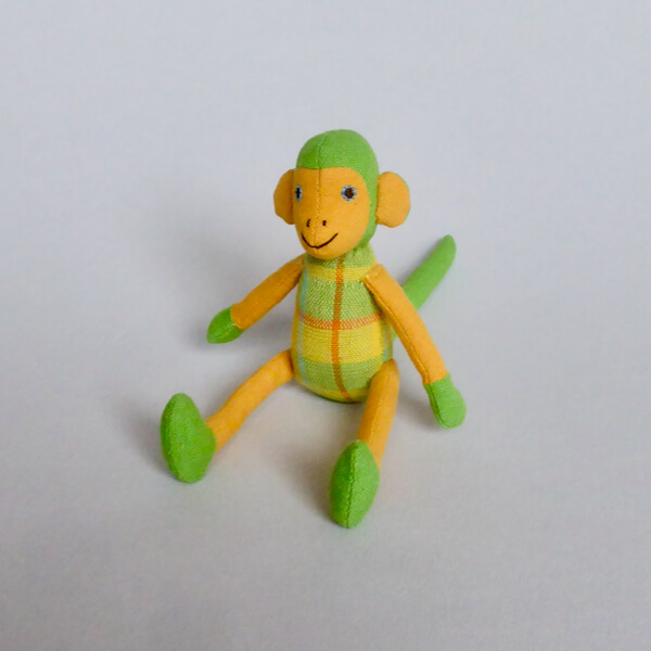 Sittande apa i grönt, orange och gult tyg, klargröna händer och fötter. Vänligt ansikte. Charmig som maskot! Fair TrADE.