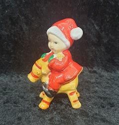 Äldre tomte som sitter på en julbock i porslin