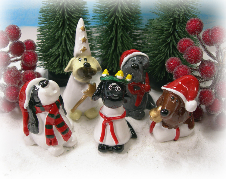 Hundfigurer med luciatågsdräkter framför små julgranar.