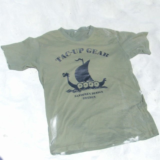 Laying in the fine white sand is a T-Shirt Khaki Green TUG.