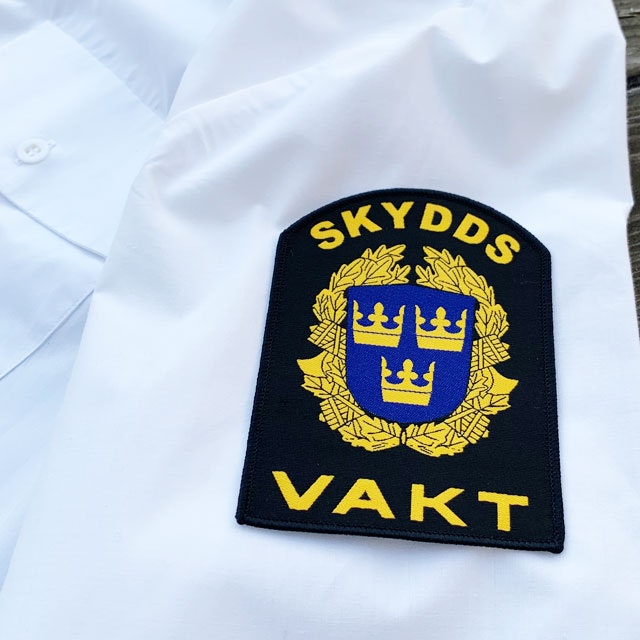 Skyddsvakt Rundad Tygmärke på ärm mot vit skjorta