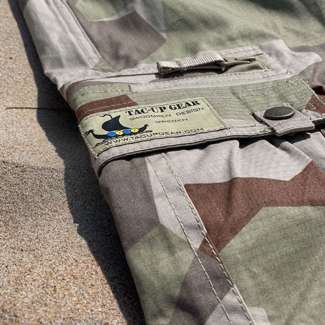 TAC-UP GEAR logo on a pair of Camp Shorts M90K Desert lying flat in the sand
