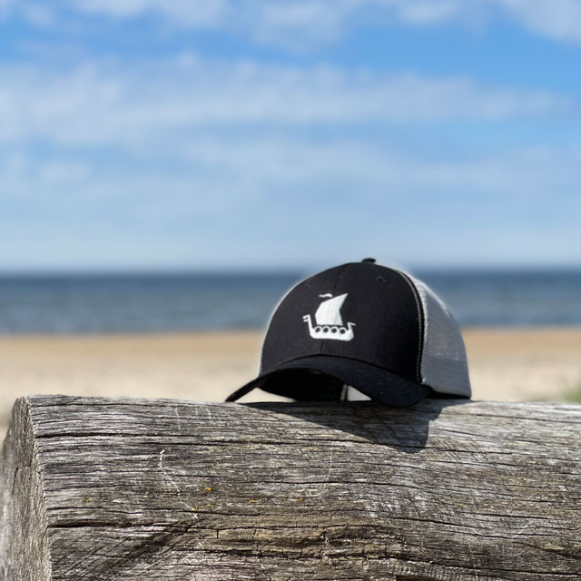 Mesh Cap Black and Grey from TAC-UP GEAR seen from the front on a log on a beach
