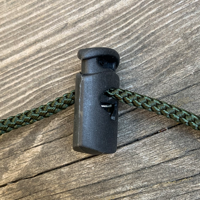 Cord Lock Matt Black photo with green string through it laying on a wooden floor