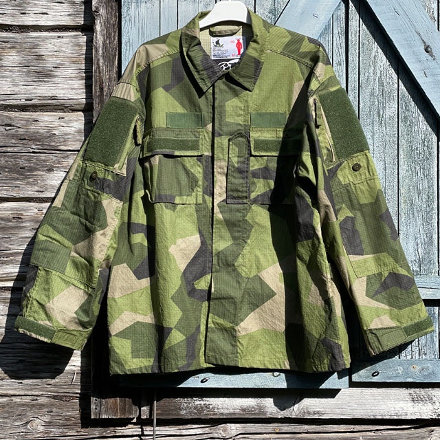 Seen full front is our popular Field Shirt M90 hanging on a wooded buildning as background