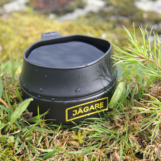 Filled to the brim the Folding Cup JÄGARE Black/Yellow/Black sits on the ground in Sweden during summer picture.