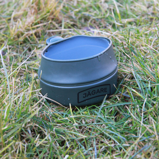 A Folding Cup JÄGARE OD Black/Green/Black filled to the brim on the grassy Swedish summer nature floor.