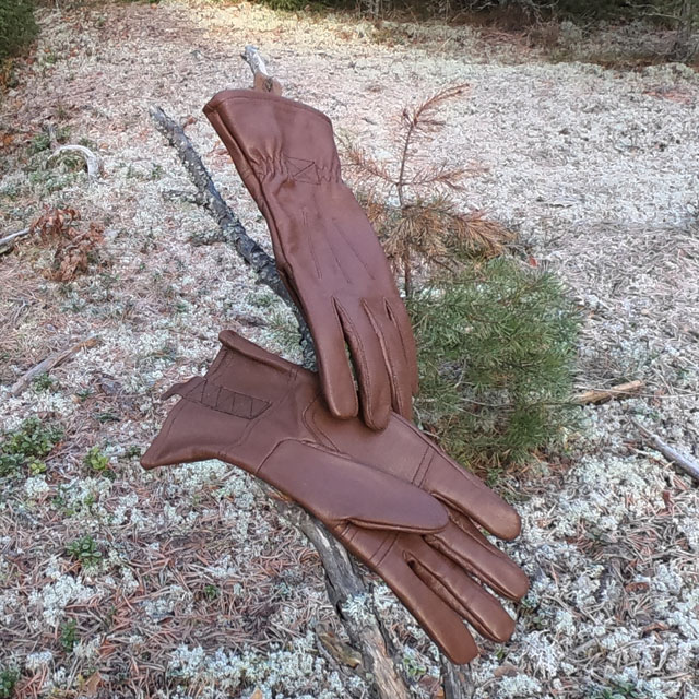 A pair of Bushcraft Leather Glove Brown from TAC-UP GEAR on a tree branch