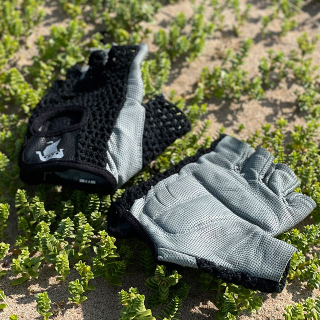 A pair of Training Glove Net Black lying flat on the sandy ground seen from a slight angle