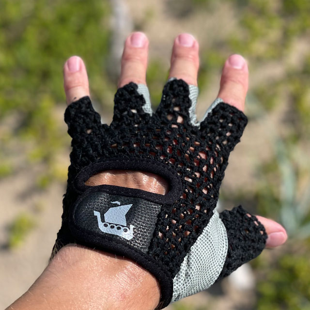 The top side of a Training Glove Net Black with beach sand and green background
