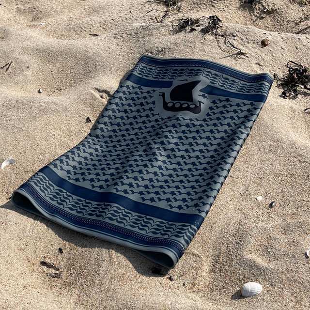 A Neck Tube Shemagh Navy Grey from TAC-UP GEAR lying flat on a sandy beach seen from a slight angle