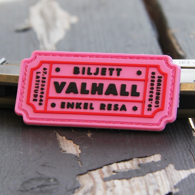 Ett Biljett Valhall PVC Rosa märke mot en bakgrund i trä.