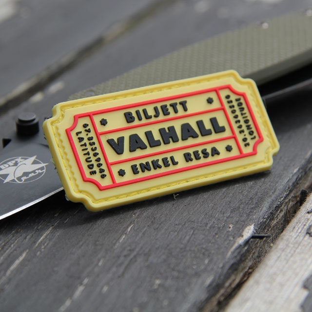 Ett Biljett Valhall PVC Gul/Röd märke med en kniv i bakgrunden för storleksjämförelse.