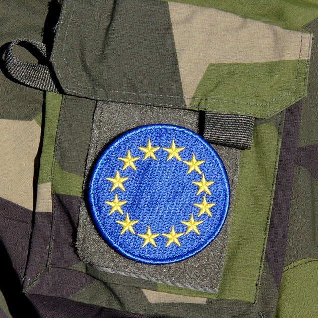 A mounted EU Blue Embroidered Patch on a M90 camouflage jacket sleeve.