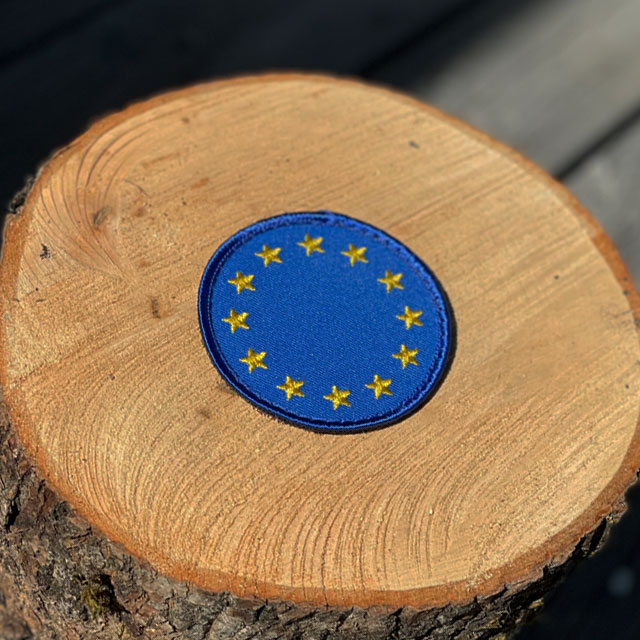 EU Round Blue Hook Patch from TAC-UP GEAR with wooded background seen from an angle
