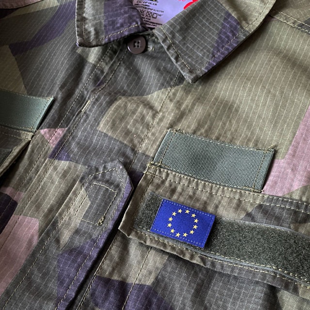 A Blue and yellow EU Flag Hook Patch Small from TAC-UP GEAR on a M90 shirt breast loop seen from a distance