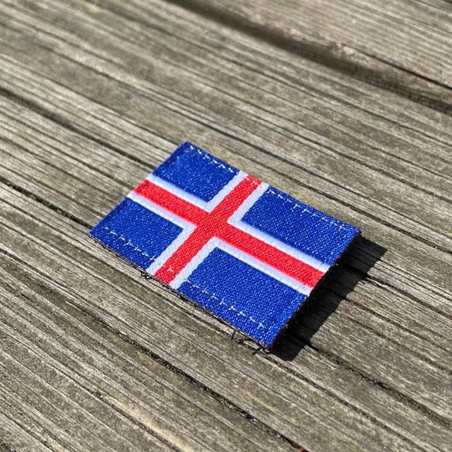 A Iceland Flag Hook Patch Small from TAC-UP GEAR laying on wooded a plank seen from an angle