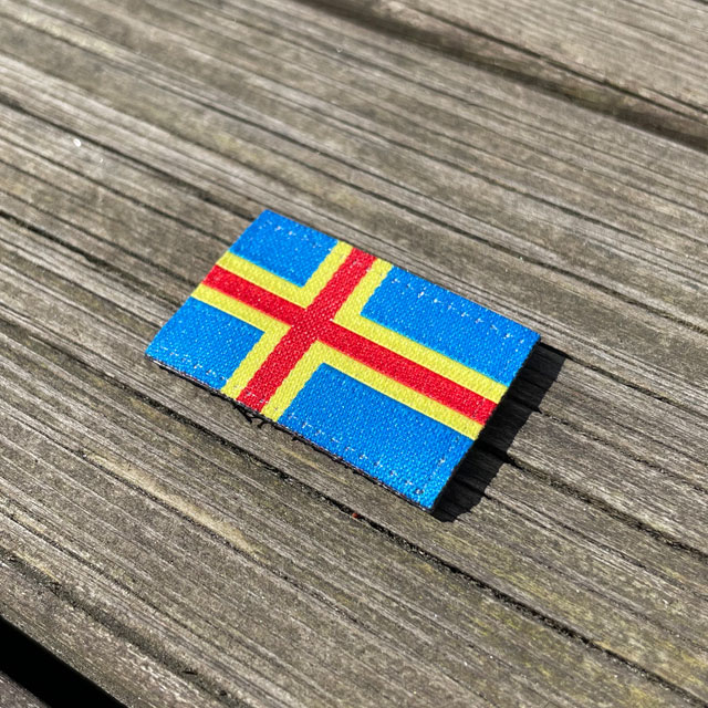A Åland Flag Hook Patch Small from TAC-UP GEAR lying flat on a wooden plank seen from an angle