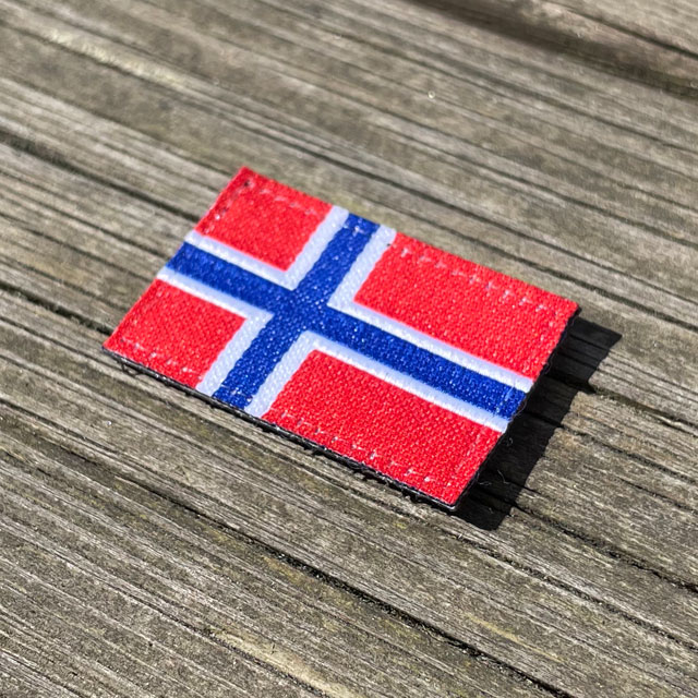 A Norway Flag Hook Patch Small from TAC-UP GEAR lying flat on wooded plank seen from an angle