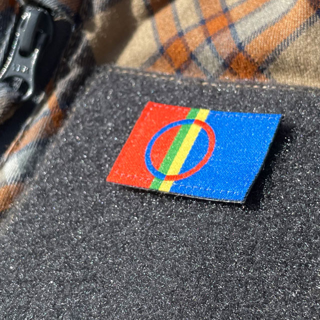 A close up picture of a Sámi Flag Hook Patch Small from TAC-UP GEAR mounted with hook and loop on a shirt sleeve