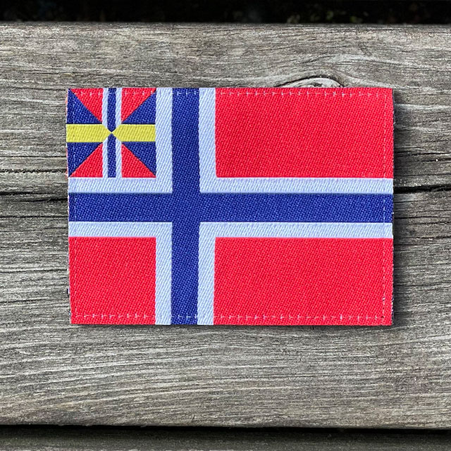 Norges handelsflagga 1844–1898/99 som ett tygmärke och som ligger på ett trägolv