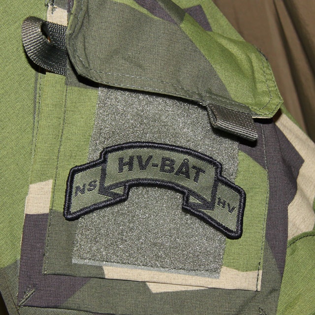 A mounted HV-BÅT Hook Scroll Patch on a M90 camouflage jacket.