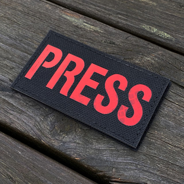 A IR - PRESS Red txt Hook Patch seen slightly from the side