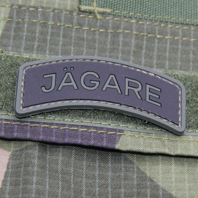 A JÄGARE Green/Black/Green PVC Patch with M90 camouflage background.