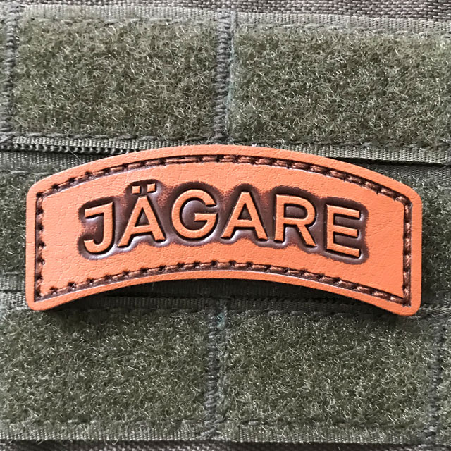 A bright and shiny JÄGARE Leather Hook Patch on green background.