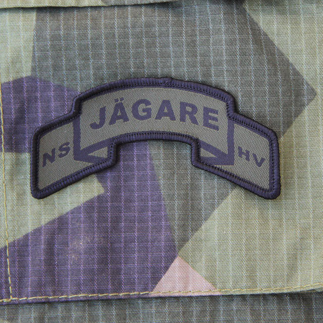 A JÄGARE Scroll Patch on a M90 Camouflage background.
